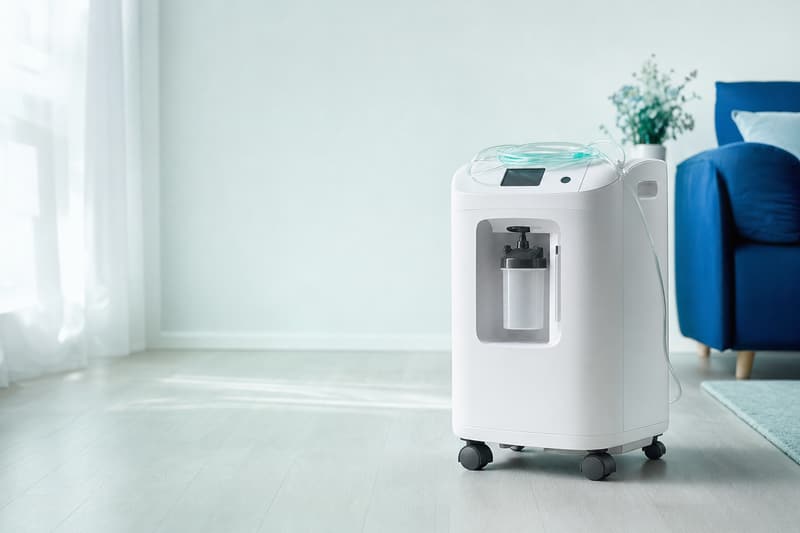 Concentrador de oxigênio branco sobre rodinhas em uma sala clara, com a cânula nasal por cima