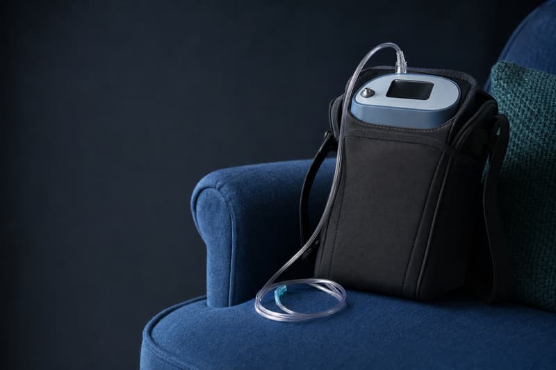 Concentrador de oxigênio portátil em uma bolsa de ombro, com a cânula nasal, sobre uma poltrona