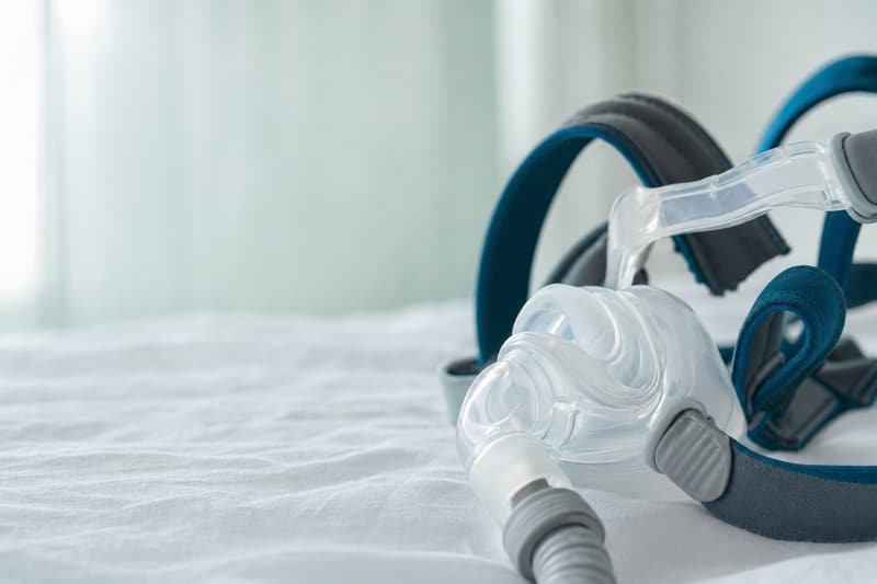 Detalhe de uma máscara de CPAP com almofada de silicone e tiras acolchoadas sobre lençol branco