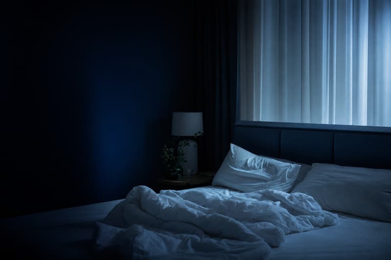 Cama vazia com lençóis amassados à noite, com a luz da lua entrando pela cortina